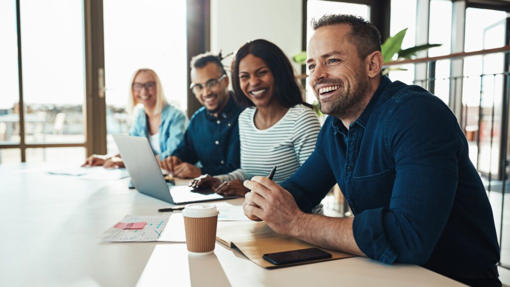 A group of professionals smiling and discussing business success in a modern office.