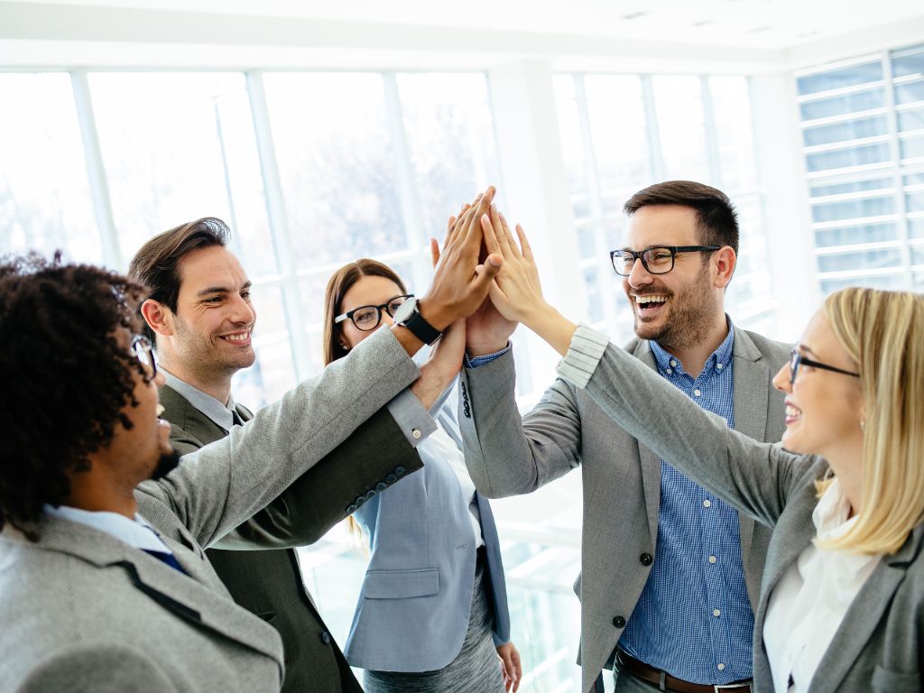 Professionals high-five in a modern office, celebrating business success.